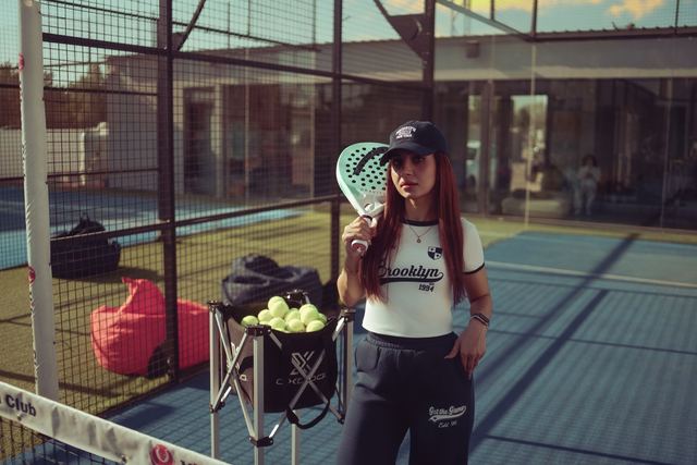 Joueur derrière la paroi vitrée d'un court de padel, surface bleue et fixations visibles